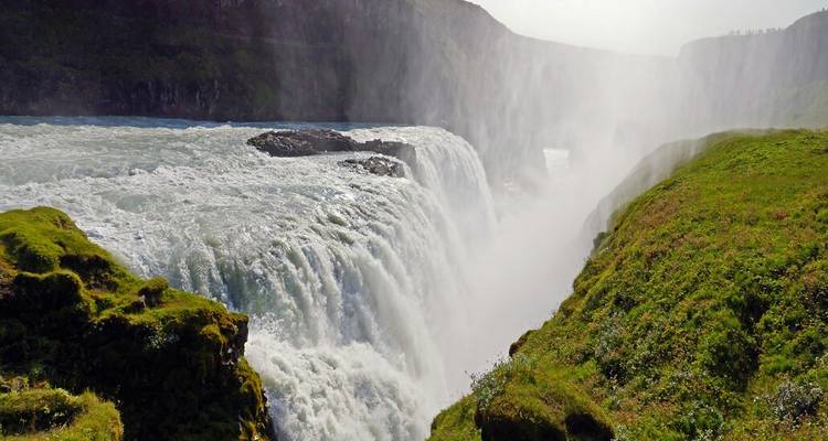 La puissante cascade de la chute d'eau de Gullfoss s'écrase à travers un canyon verdoyant dans la brume et la lumière du soleil.