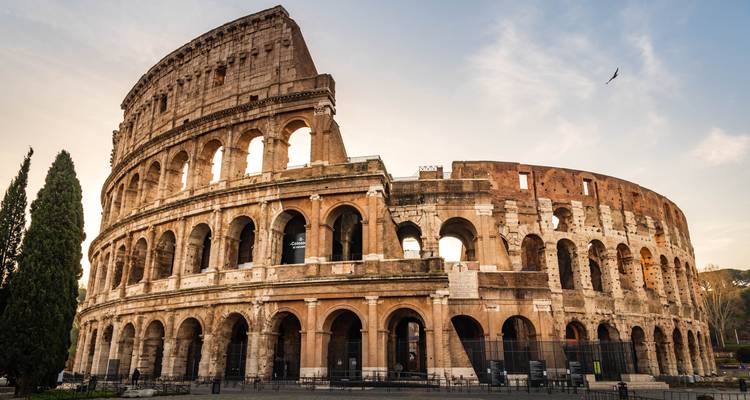 Iconic Colosseum of Rome bathed in warm evening light against a pale sky.