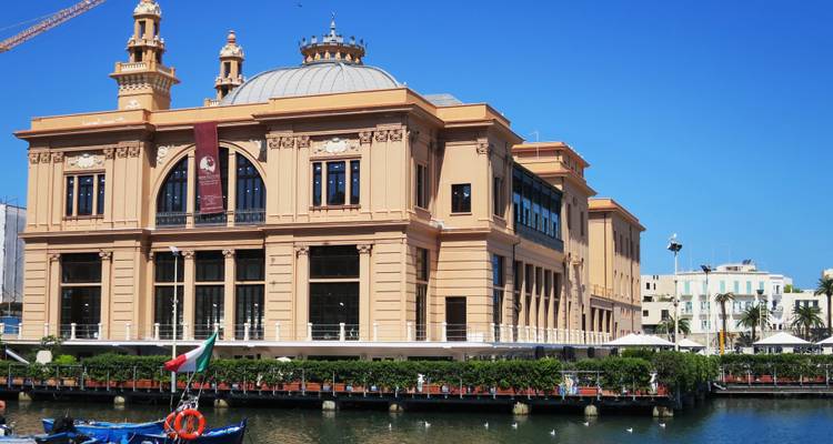 Historic Teatro Margherita building reflected in Bari harbor under bright blue sky.