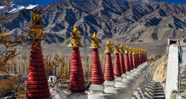 Line of red and gold stupas set before dramatic barren mountains.