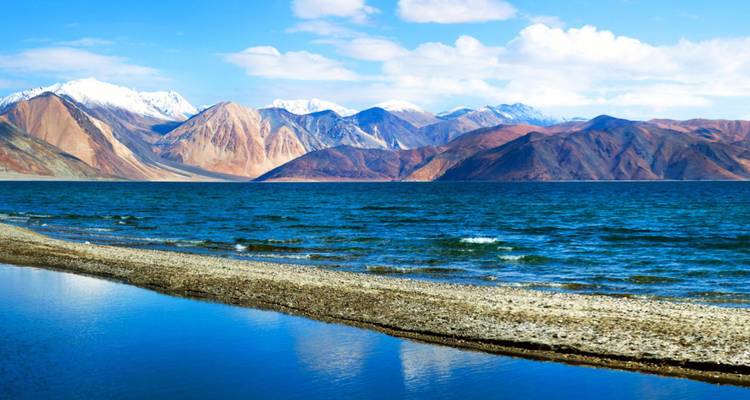 Crystal blue Pangong Lake reflecting snow-capped mountains under a bright sky.