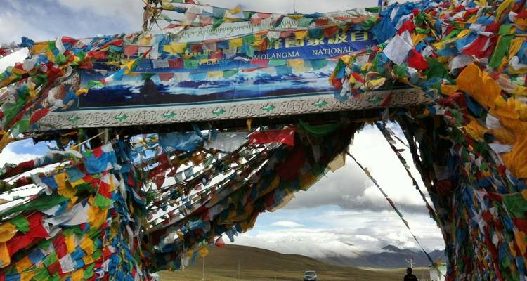Archway covered in fluttering multi-colored prayer flags at a high mountain pass.