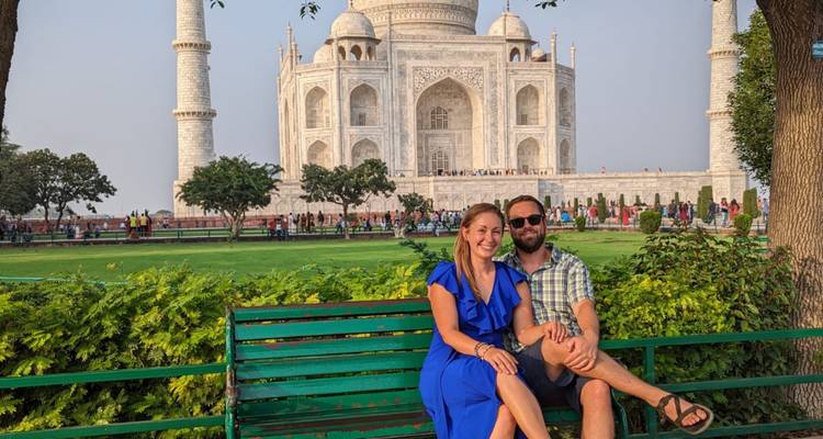Happy couple sitting on a bench with the Taj Mahal rising majestically behind them.