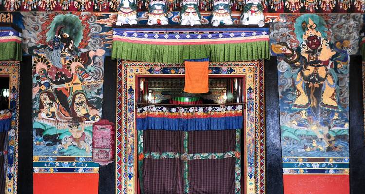 Intricately painted entrance of a Buddhist monastery with vibrant murals and hanging fabric.