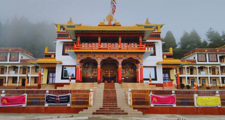 Buddhist monastery with ornate façade emerging from morning fog against a forested backdrop.