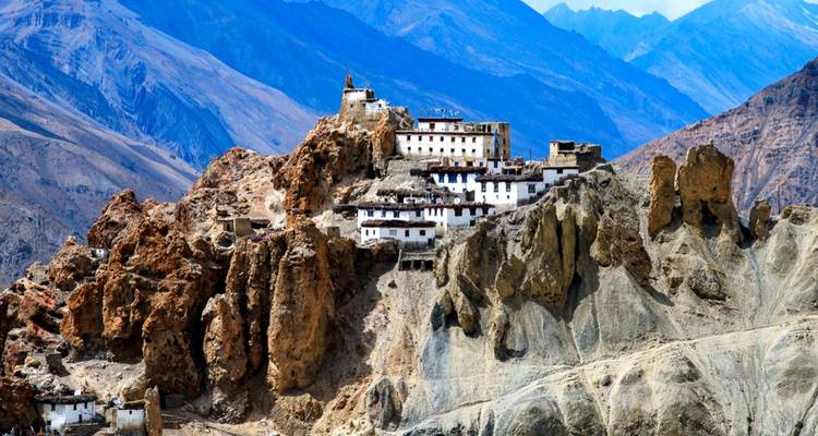 Monastery perched dramatically on rugged ochre cliffs with barren mountain ranges behind.