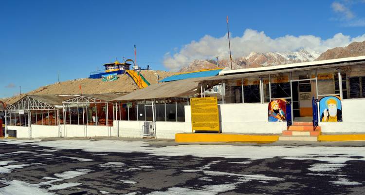 Roadside shrine and rest stop painted in bright colors set against arid mountains under a blue sky.