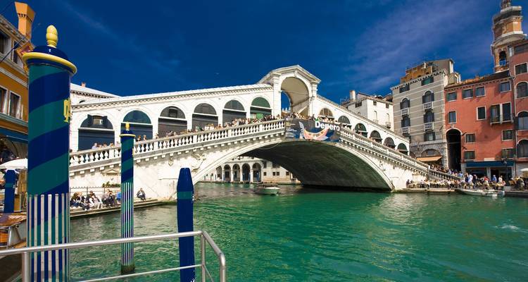 Ikonische weiße Marmorbrücke Rialto, die sich über die smaragdgrünen Gewässer Venedigs erstreckt, mit Menschenmassen und blauem Himmel