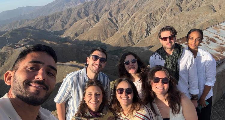 Group selfie on a high lookout with rugged Atlas mountain ridges sprawling behind.