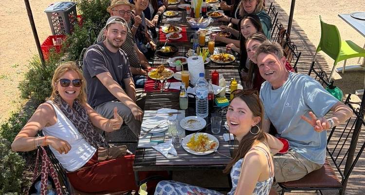 Large travel group share a cheerful outdoor meal around a long table filled with Moroccan dishes.
