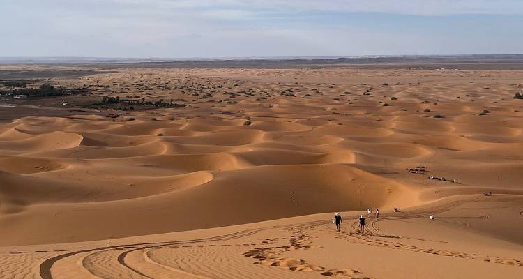 Endless rolling sand dunes stretch to the horizon with tiny figures trekking across.