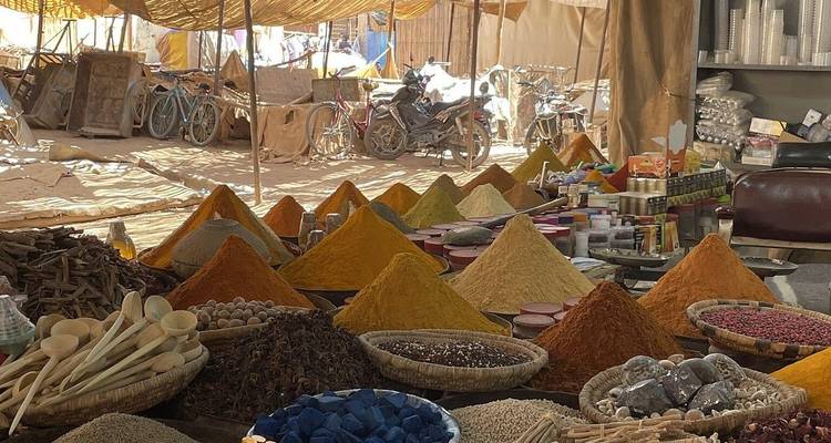 Colorful conical piles of spices and herbs fill a bustling market stall under a canvas roof.