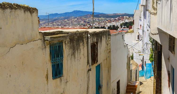 Paredes encaladas y desgastadas con bordes azules en una calle de la ladera con vista a un pueblo marroquí.