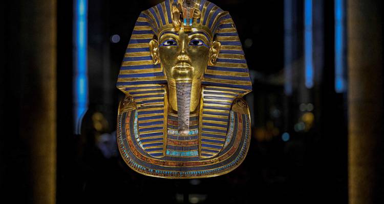 Illuminated golden mask of Tutankhamun displayed in a dark museum setting.