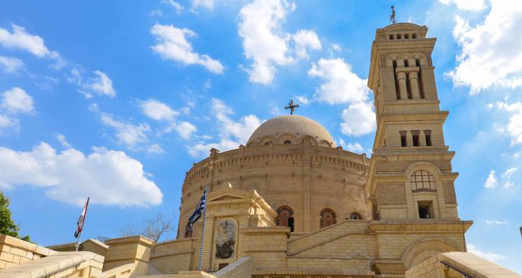 Sand-colored domed church with a tall bell tower set against a bright blue sky.