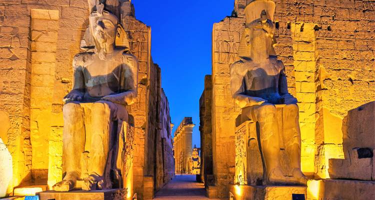 Dramatically lit seated statues at Luxor Temple during blue hour.