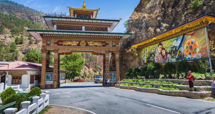 Colorful ornamental gate marking the entrance to Bhutan, set against rocky hills and murals.