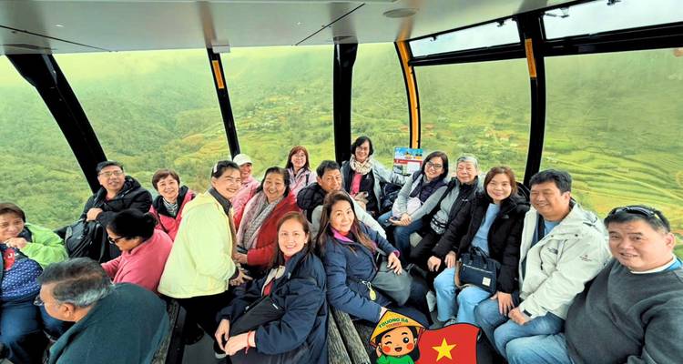 Large tour group inside cable car cabin with Vietnam cartoon sticker overlay.