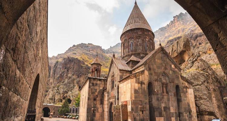 Stone Geghard Monastery set in a dramatic cliff valley framed by an archway.