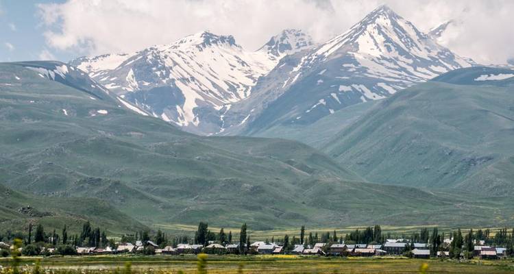 Snow-capped Armenian mountains rise above a green valley dotted with a small village.
