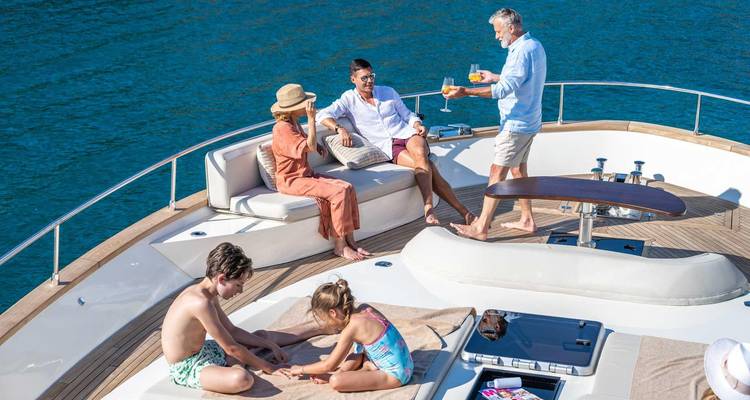 Une famille multigénérationnelle se détend autour de boissons sur le pont ensoleillé d'un yacht privé au-dessus d'une eau bleue.