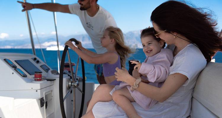 La mère tient un jeune enfant tandis que les enfants aident à naviguer un bateau sur une mer bleu clair.