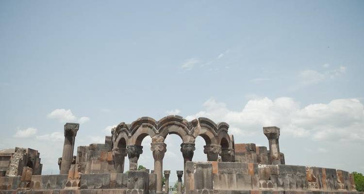Stone ruins of arched basilica columns against pale blue sky with scattered clouds.