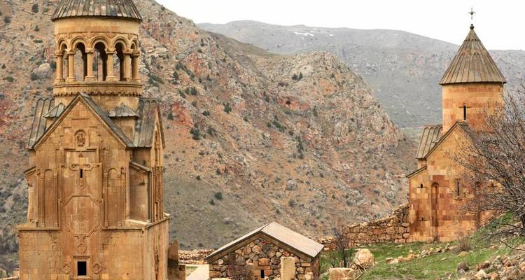 Twin medieval churches built of reddish stone set among steep rocky canyon slopes.