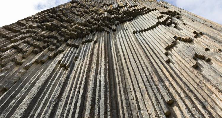 Dramatic basalt column cliff face rising vertically, showing natural stone organ-pipe formations.