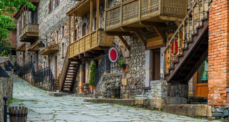 Cobblestone street lined with historic stone houses featuring wooden balconies and staircases.