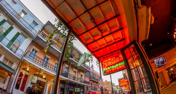 Colorful neon signs and wrought-iron balconies line a lively street scene captured with a wide-angle lens.