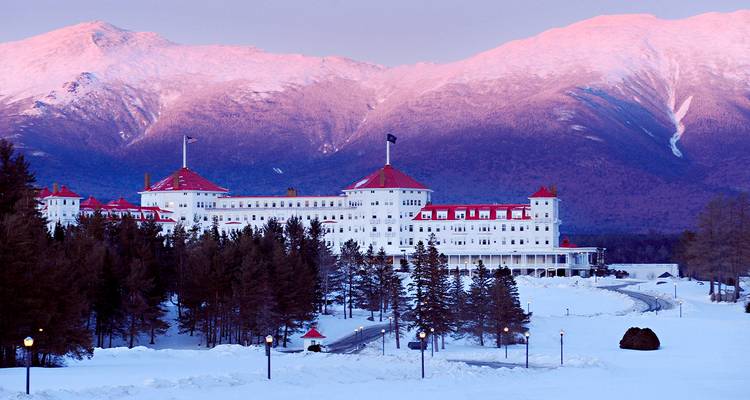 Snow-covered Mount Washington Resort framed by pine trees with rosy alpine glow on surrounding peaks.