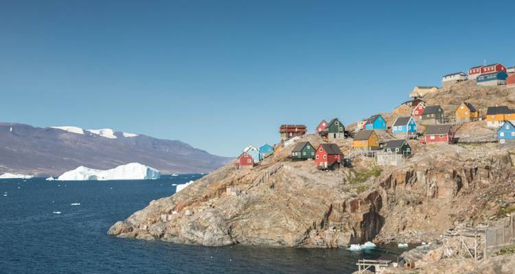 Abhang mit farbenfrohen nordischen Häusern überblickt einen eisbergübersäten Fjord unter klarem blauen Himmel.