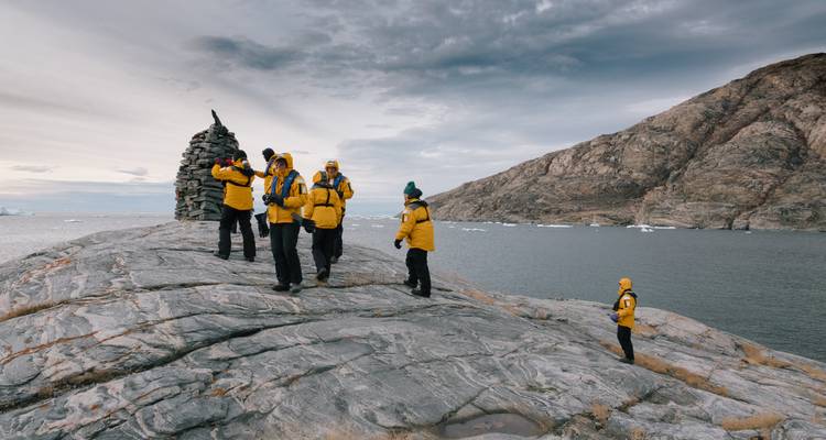 Expeditionsgruppe in einheitlichen gelben Jacken erkundet ein felsiges Kap mit Blick auf eine von Eisbergen geprägte Bucht.