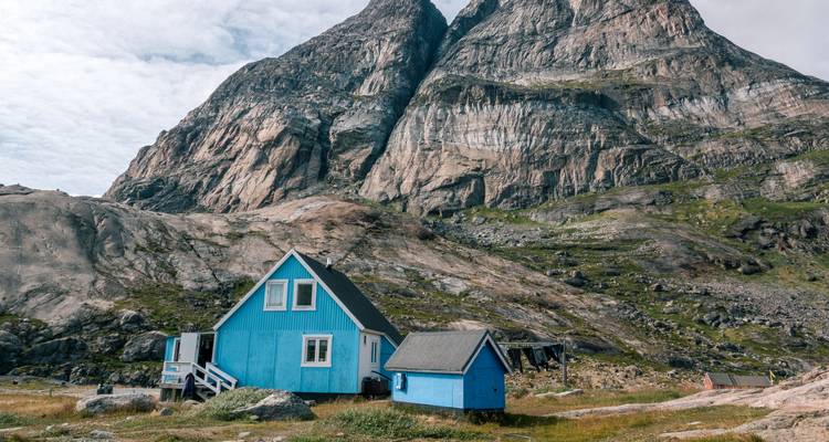 Bright blue cabin sits beneath towering granite peaks in Greenland’s remote interior.