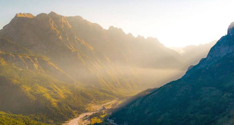 Vallée alpine spectaculaire avec des pics escarpés et des rayons de brume matinale illuminant une rivière en contrebas