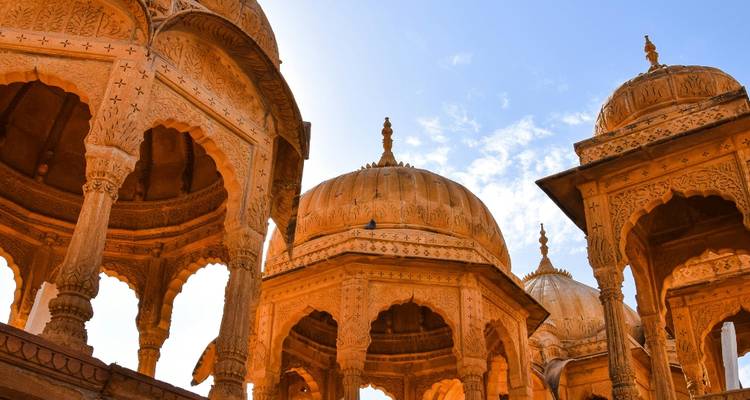 Glänzende goldene Chhatri-Kenotaphe in warmem Sonnenlicht vor blauem Himmel.