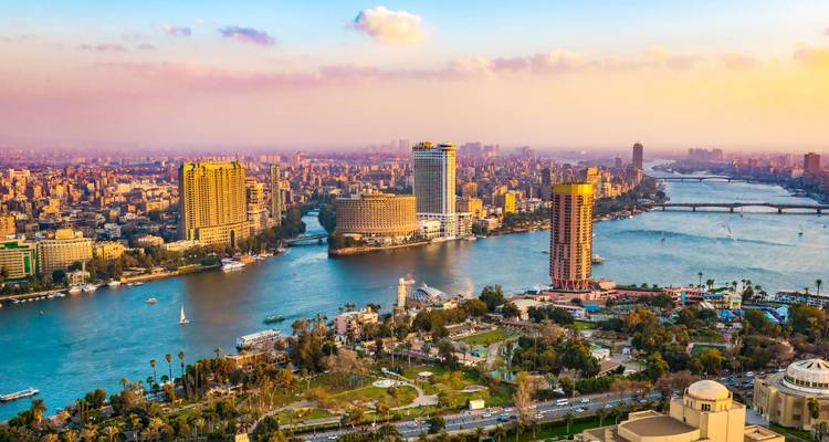 Aerial sunset view of Cairo skyline with Nile River and modern high-rise buildings.