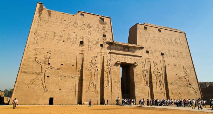 Massive sandstone pylon of Edfu Temple adorned with hieroglyphic reliefs and visitors below.