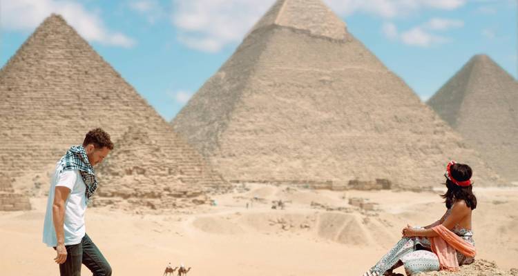 Couple poses near the Giza pyramids with desert sands and iconic triangles rising behind.