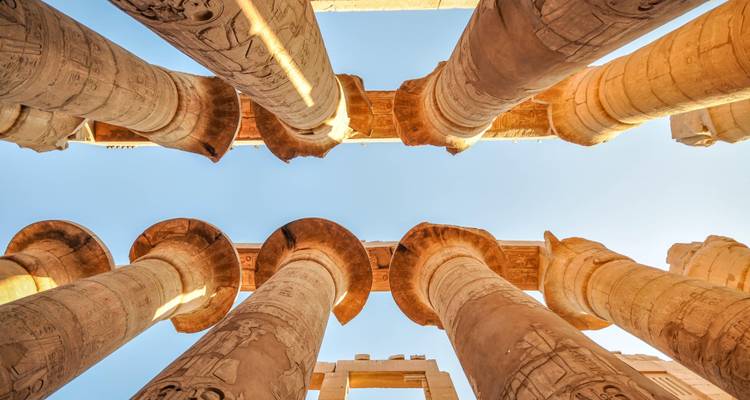 Upward angle of towering columns at Karnak Temple glowing in warm light against blue sky.