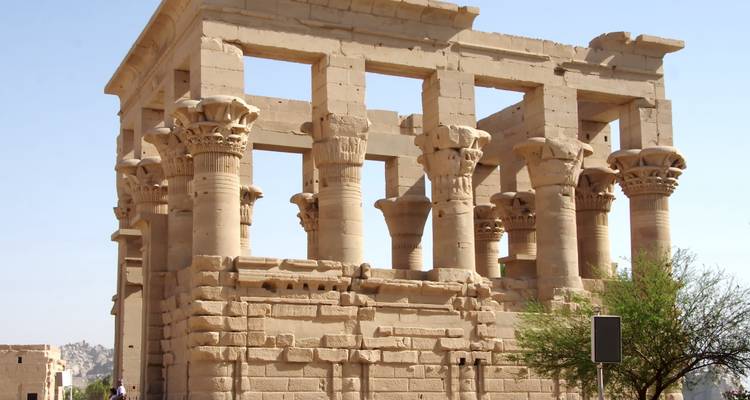 Ancient sandstone temple ruins with tall ornate columns under a clear blue sky.