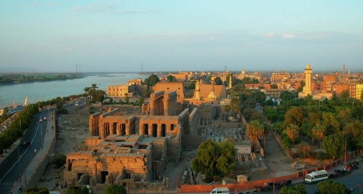Aerial view of Luxor Temple complex beside the Nile River and surrounding cityscape at dusk.