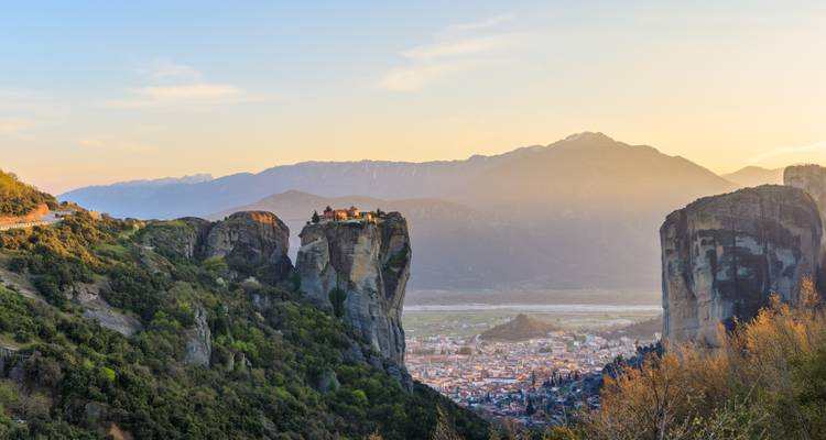 Dramatic monasteries perch atop sheer sandstone pillars above a valley at sunrise.