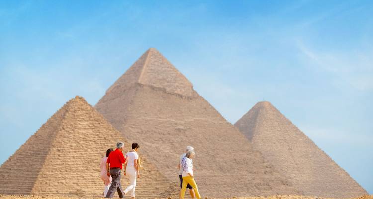 Travelers walking toward the iconic pyramids of Giza under a bright blue sky.