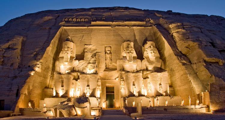 Illuminated façade of Abu Simbel Temple at twilight carved into a rock cliff.