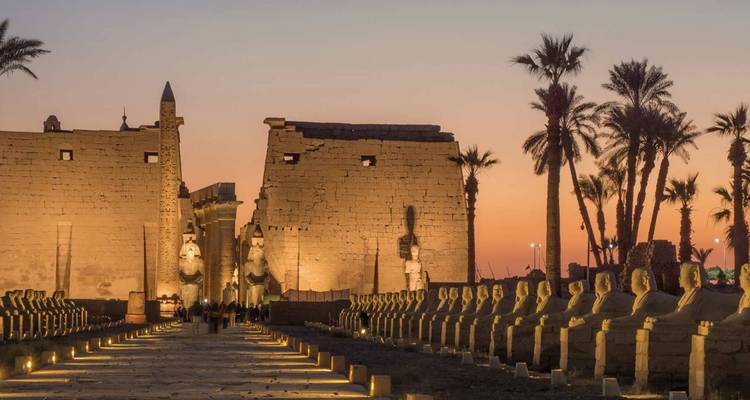 Luxor Temple avenue of sphinxes glowing under sunset skies with illuminated pylons.
