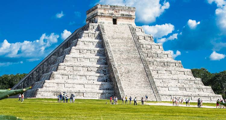 Iconic pyramid of Chichen Itza rises above manicured green lawn under bright sky