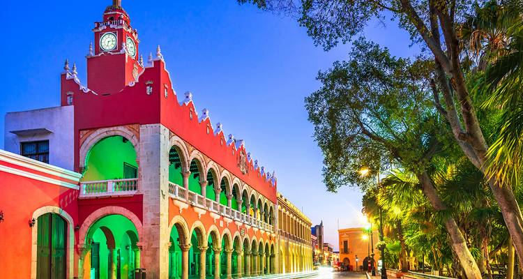 Colorfully lit colonial municipal palace lines Merida’s main square at dusk