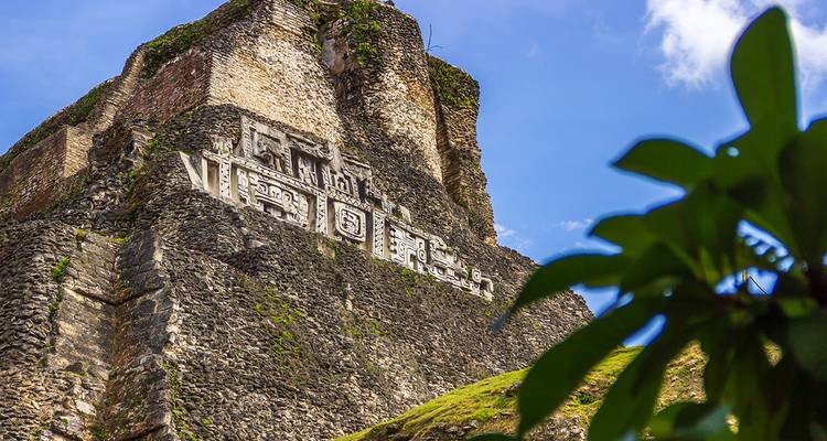 Detailed carved frieze adorns towering Maya pyramid of Xunantunich against blue sky